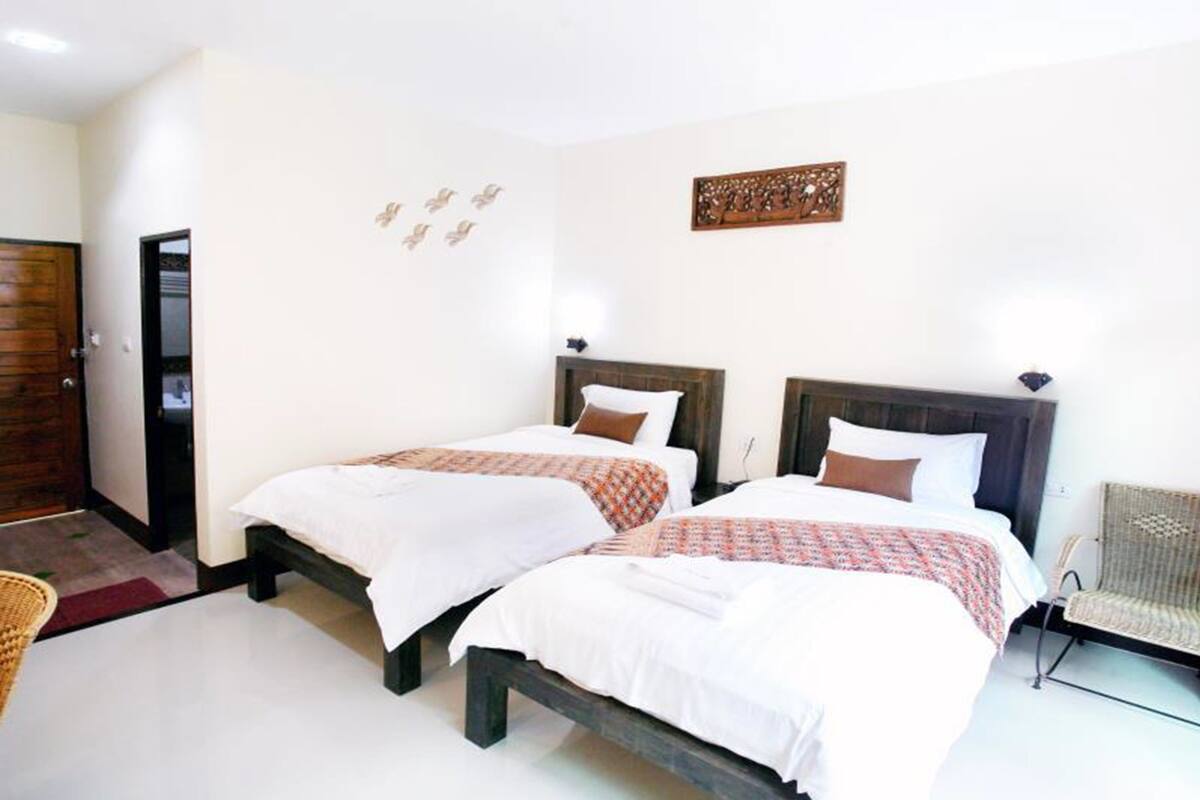 A hotel room with two beds, a wooden door, a wicker chair, and a decorative wall piece.