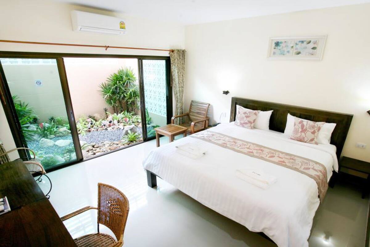 A hotel room with a large bed, a desk, a chair, and a view of a garden through a sliding door.