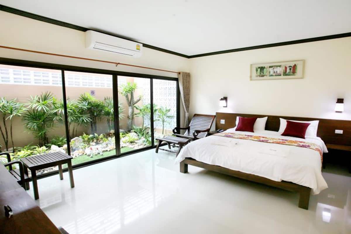 A hotel room with a large sliding glass door leading to a garden, a bed with white bedding, two wooden chairs, and a small table.