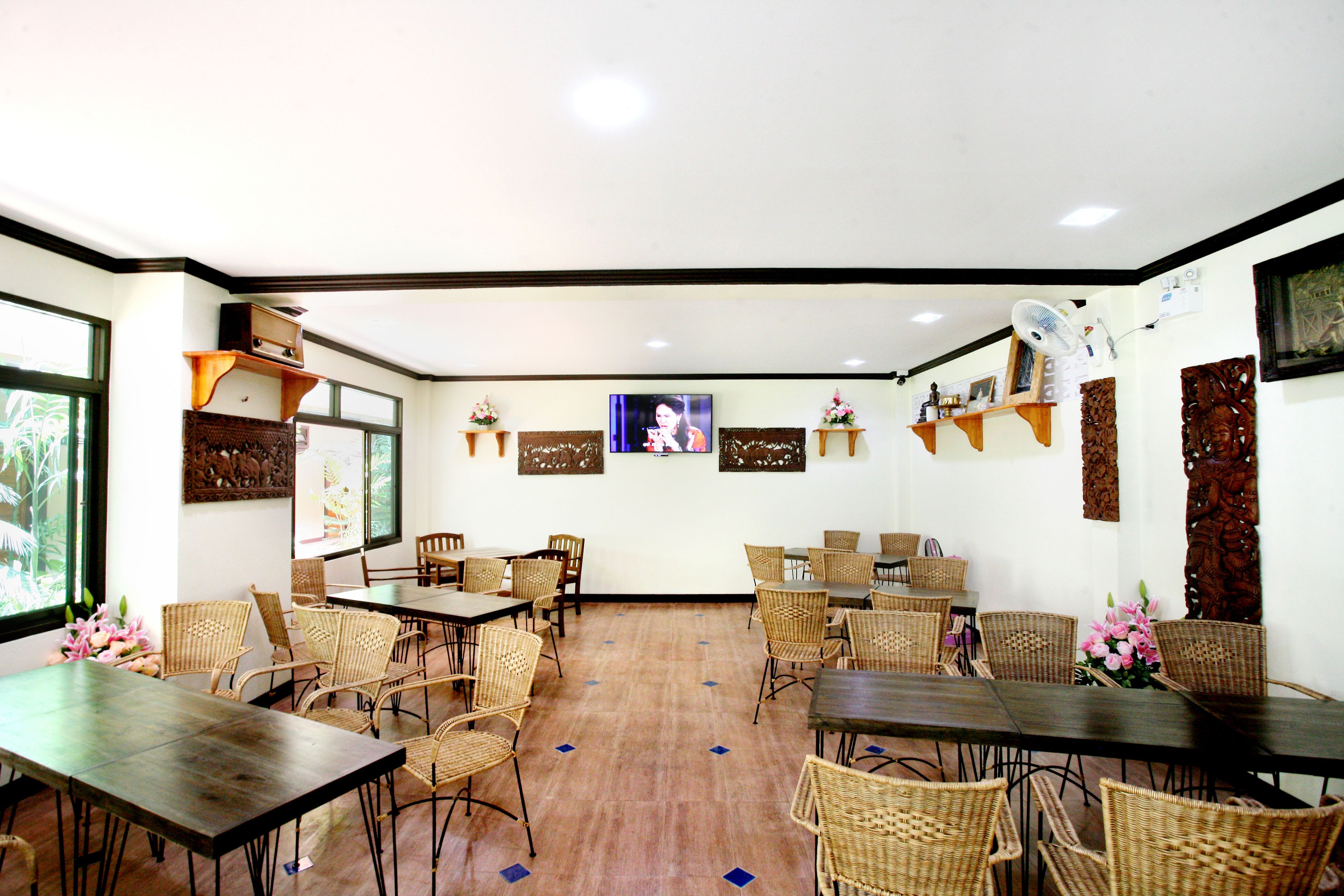 A dining area with wicker chairs, wooden tables, and a large TV screen.