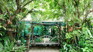 A wooden swing set in a lush garden with dense foliage and a variety of plants. - Baan Na Khon Hotel (Nakhon Si Thammarat)