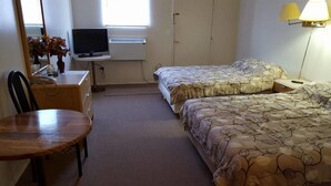 Habitación de hotel con dos camas, un escritorio con computadora, una silla, una lámpara y un ventanal.