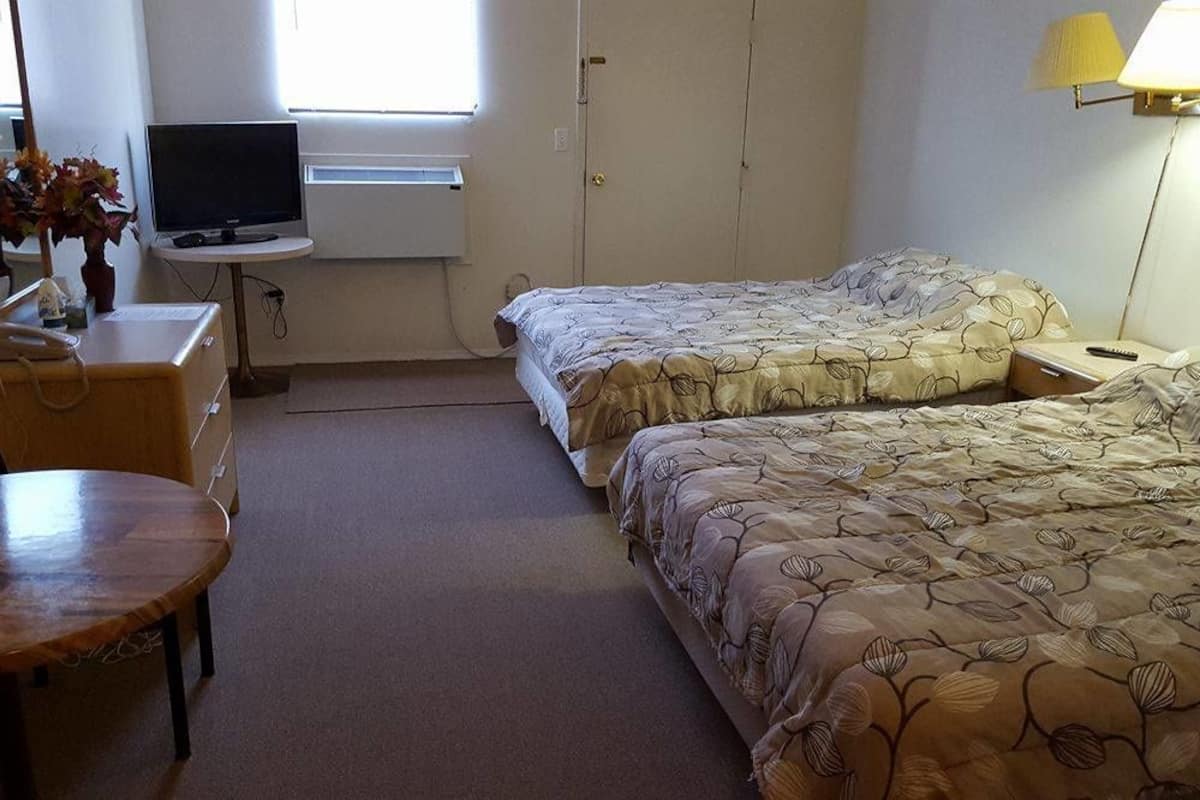 A hotel room with two beds, a desk with a computer, a chair, a lamp, and a window.