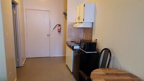 Una cocina compacta con una puerta blanca, una estufa, un fregadero y una silla negra.