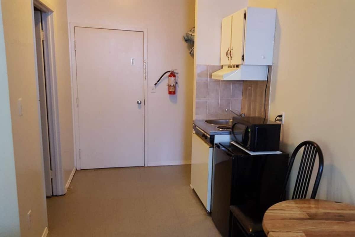 A compact kitchen with a white door, a stove, a sink, and a black chair.