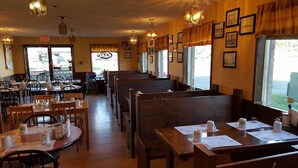 Un interior de restaurante con mesas y bancos de madera, fotografías enmarcadas en las paredes y vistas a través de las ventanas.