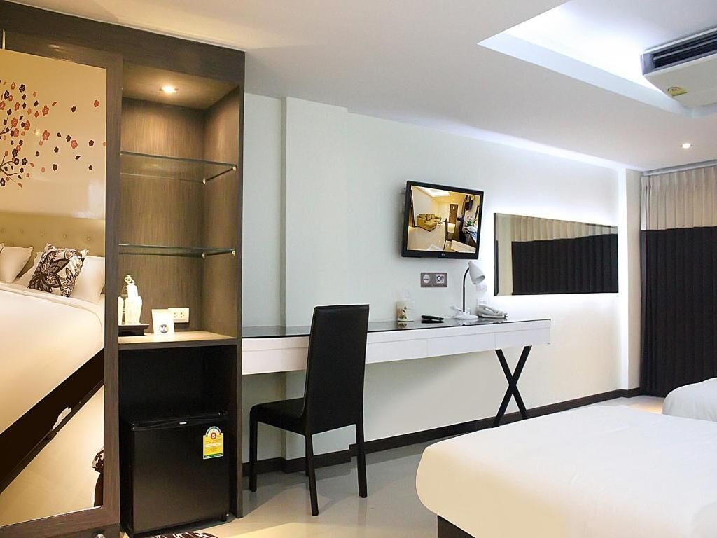A hotel room with a bed, a desk with a chair, a TV, and a wardrobe.