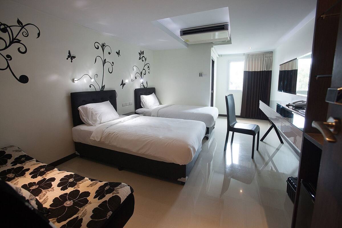 Habitación de hotel con dos camas, un escritorio, una silla, aire acondicionado y televisor.