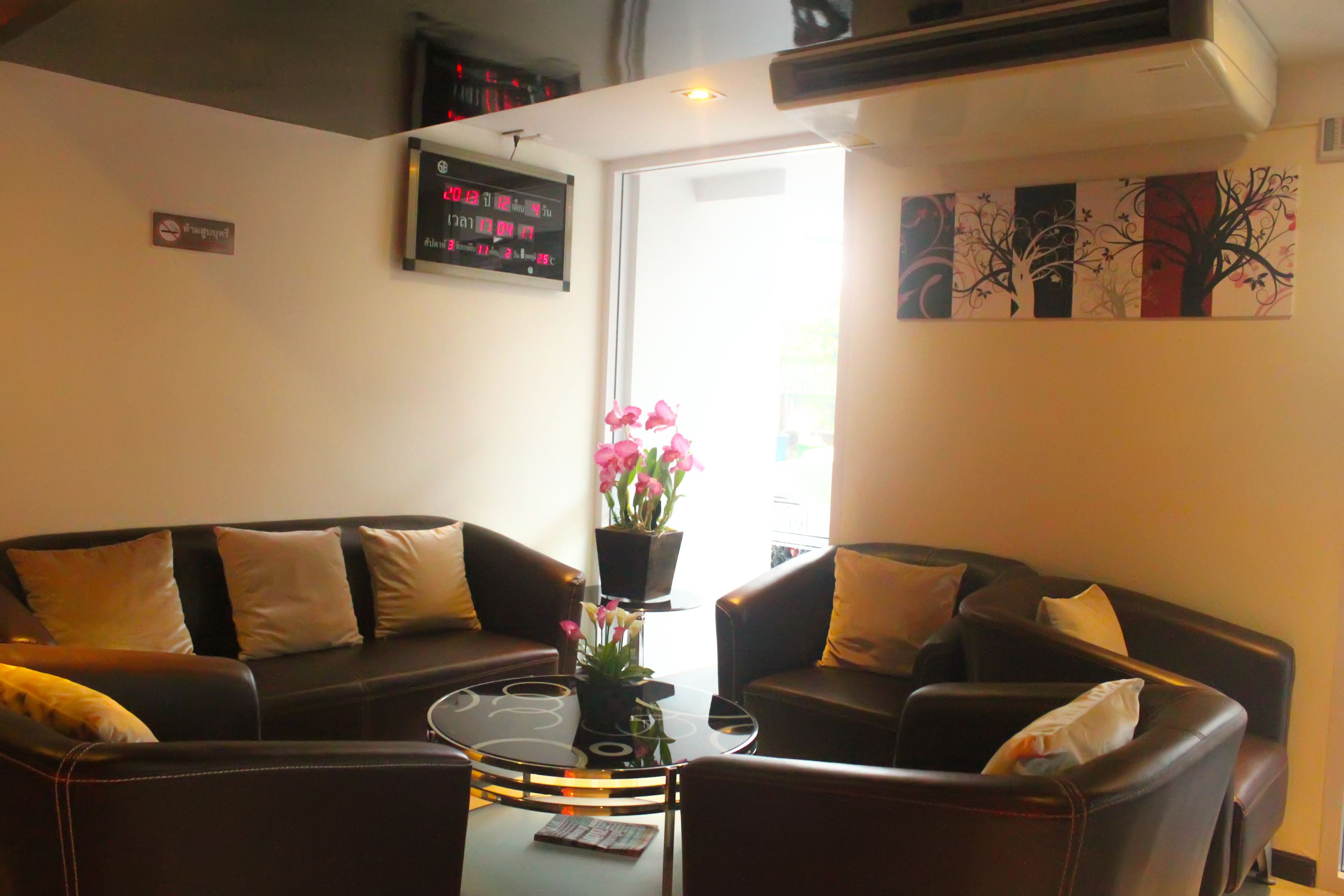 Een woonkamer met een bruine leren bank, een glazen salontafel en een potplant met roze bloemen.