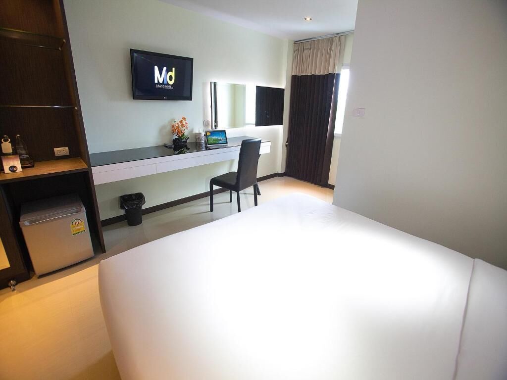 A hotel room with a bed, a desk, a chair, a TV, and a window with curtains.