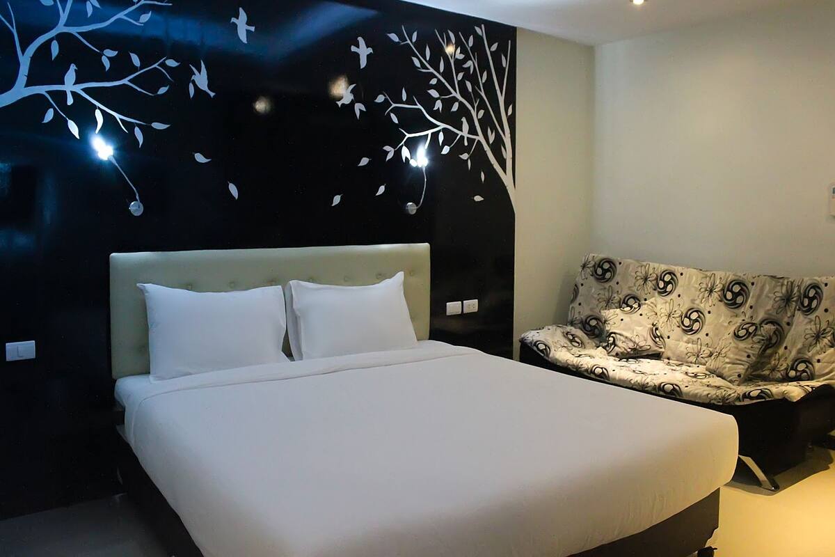 Un dormitorio moderno con una cama grande, un sofá y una pared con diseño de árbol.