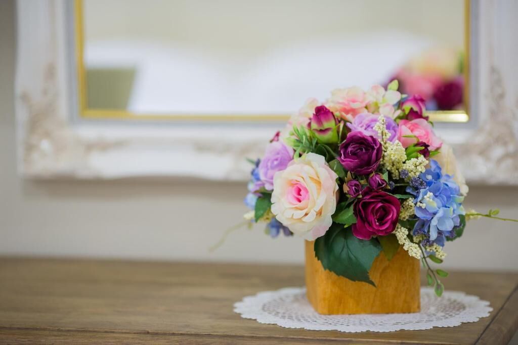 A wooden vase with a bouquet of flowers on a wooden table with a lace doily.
