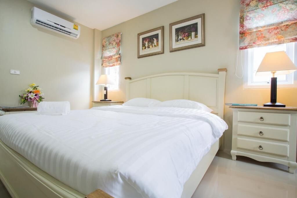 A hotel room with a large bed, two bedside tables, a nightstand, a lamp, and a window with floral curtains.