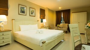 Quarto de hotel com uma cama grande, duas poltronas, uma mesinha com abajur e um guarda-roupa.