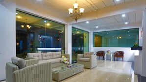 Um saguão de hotel moderno com móveis de vime, uma mesa de centro de vidro e um candelabro.