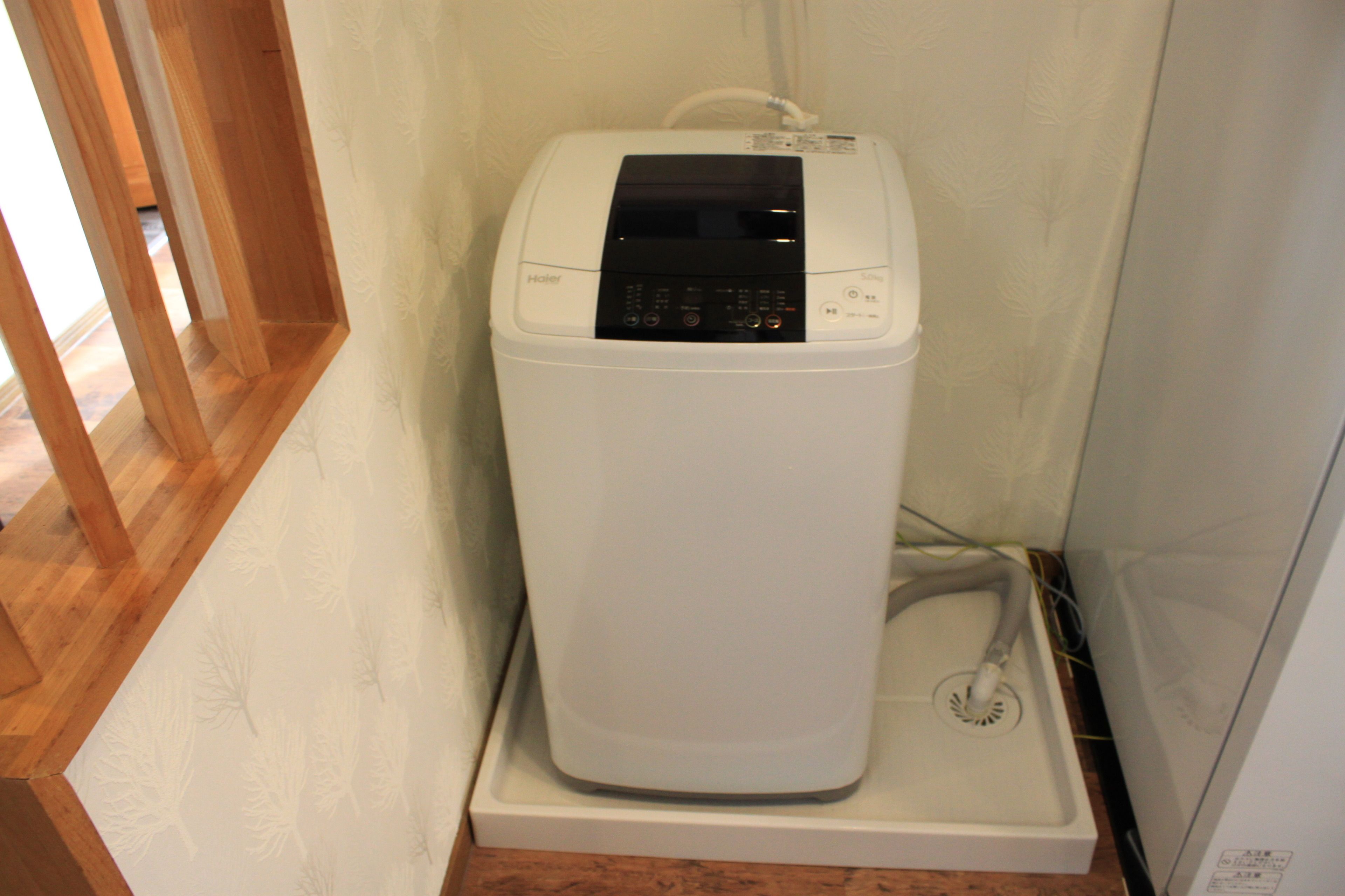 Une machine à laver compacte, blanche, fixée au mur et dotée d’un panneau de commande, située dans un coin d’une pièce au sol en bois et dont le mur est blanc.