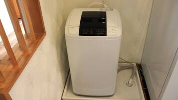 Une machine à laver compacte, blanche, fixée au mur et dotée d’un panneau de commande, située dans un coin d’une pièce au sol en bois et dont le mur est blanc.