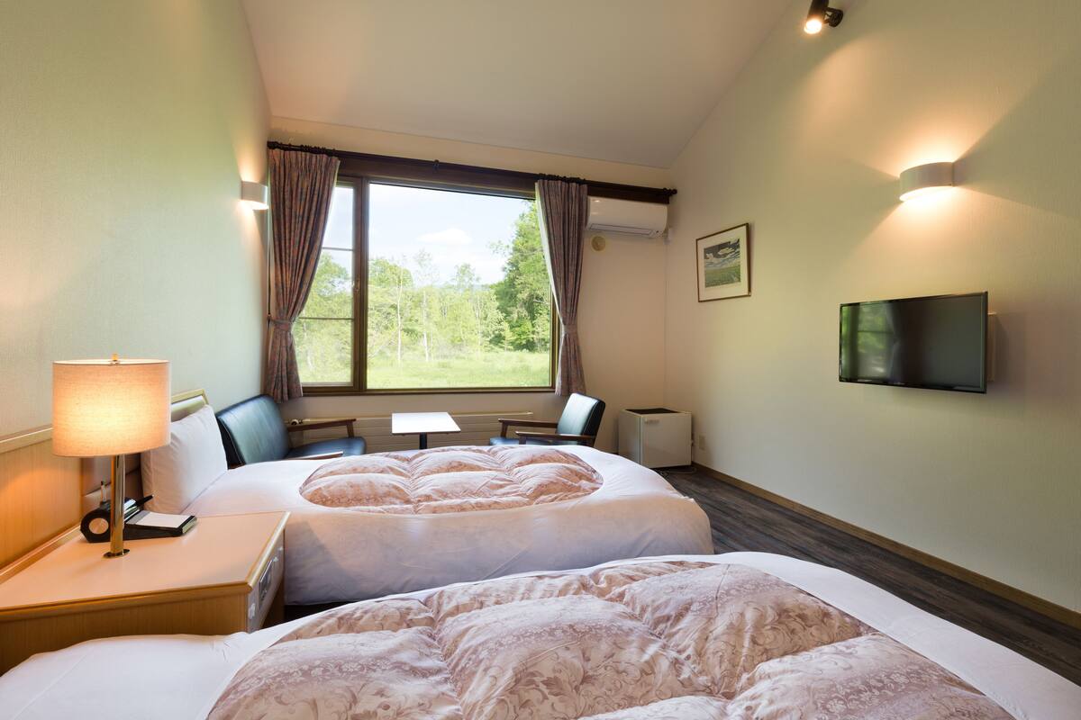 Ein Hotelzimmer mit zwei Betten, einem Schreibtisch, einem Stuhl, einem Fernseher und einem Fenster mit Vorhängen.