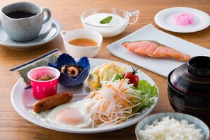 Een maaltijd met diverse gerechten, waaronder een bord met eieren, een worstje, een salade en een stuk vis op een houten tafel.