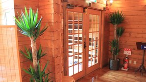 Un intérieur en bois avec une porte coulissante en verre, une petite chaise en bois et deux plantes en pot.