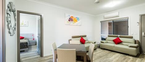 Una sala de estar moderna con una mesa de comedor, sillas de mimbre, un sofá y una almohada roja.
