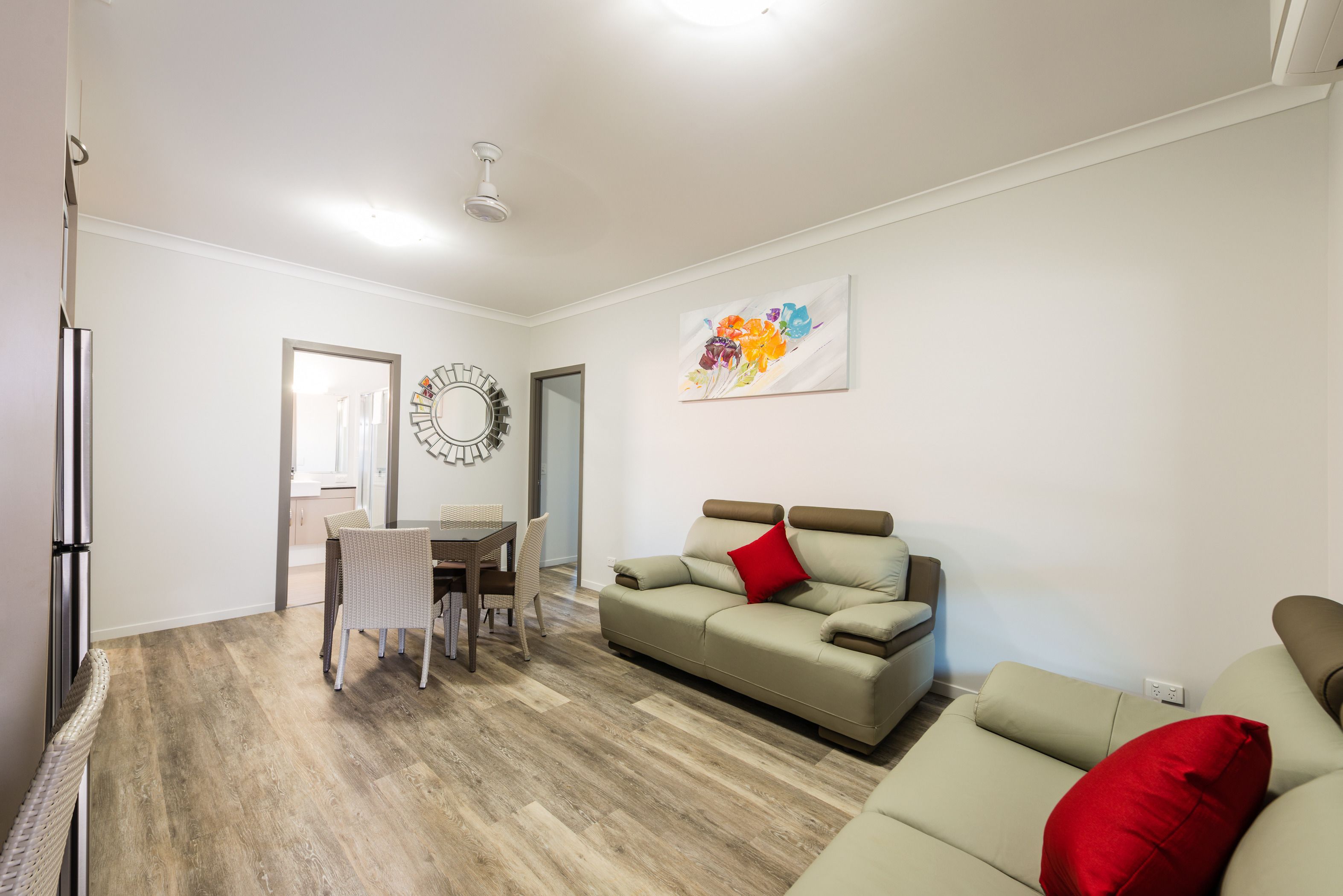A living room with a sofa, a dining table with chairs, a refrigerator, and a wall-mounted artwork.