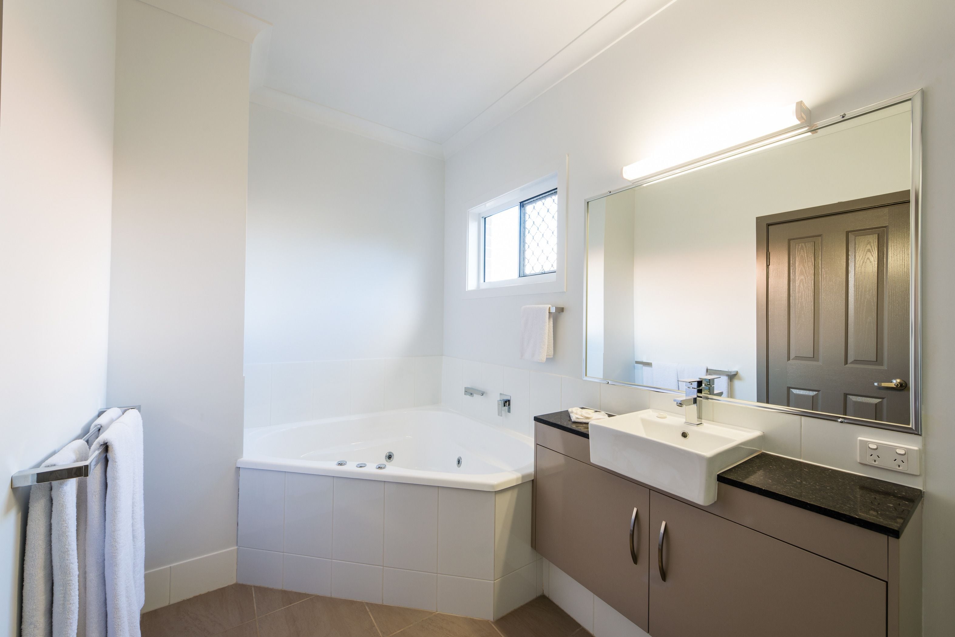 A modern bathroom with a bathtub, two sinks, a large mirror, and a window.