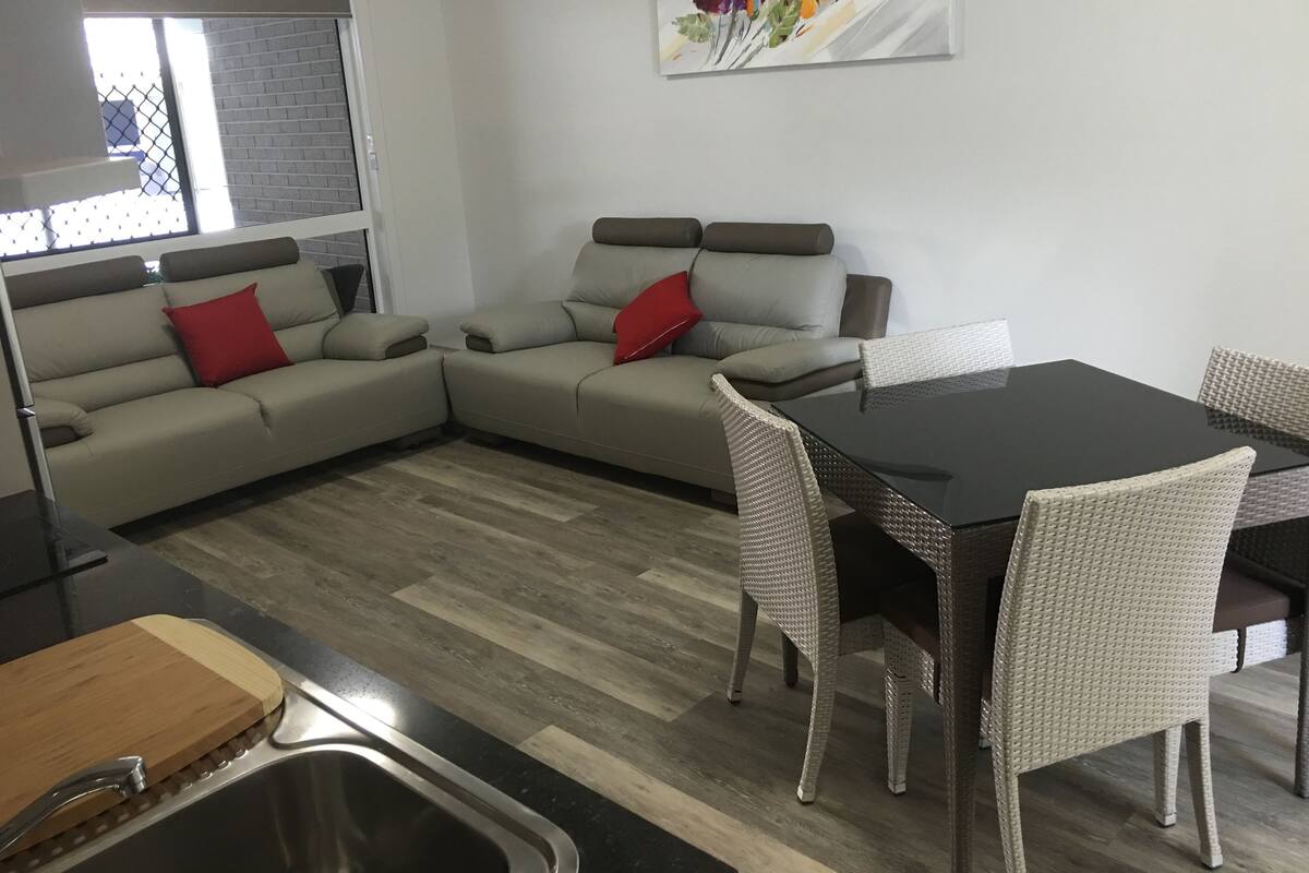 A modern kitchen with a dining area, featuring a sofa set, a dining table, and a kitchen sink.