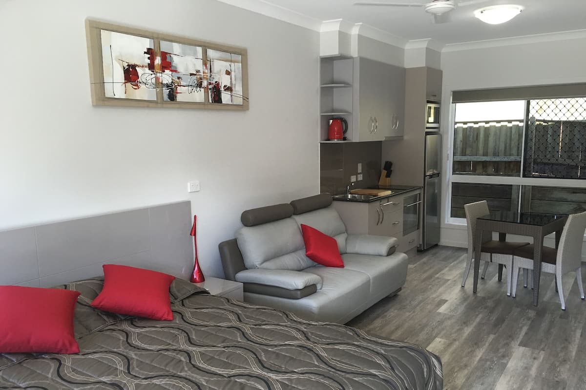 A compact living space with a sofa, a dining table with chairs, a kitchenette, and a window with a view.