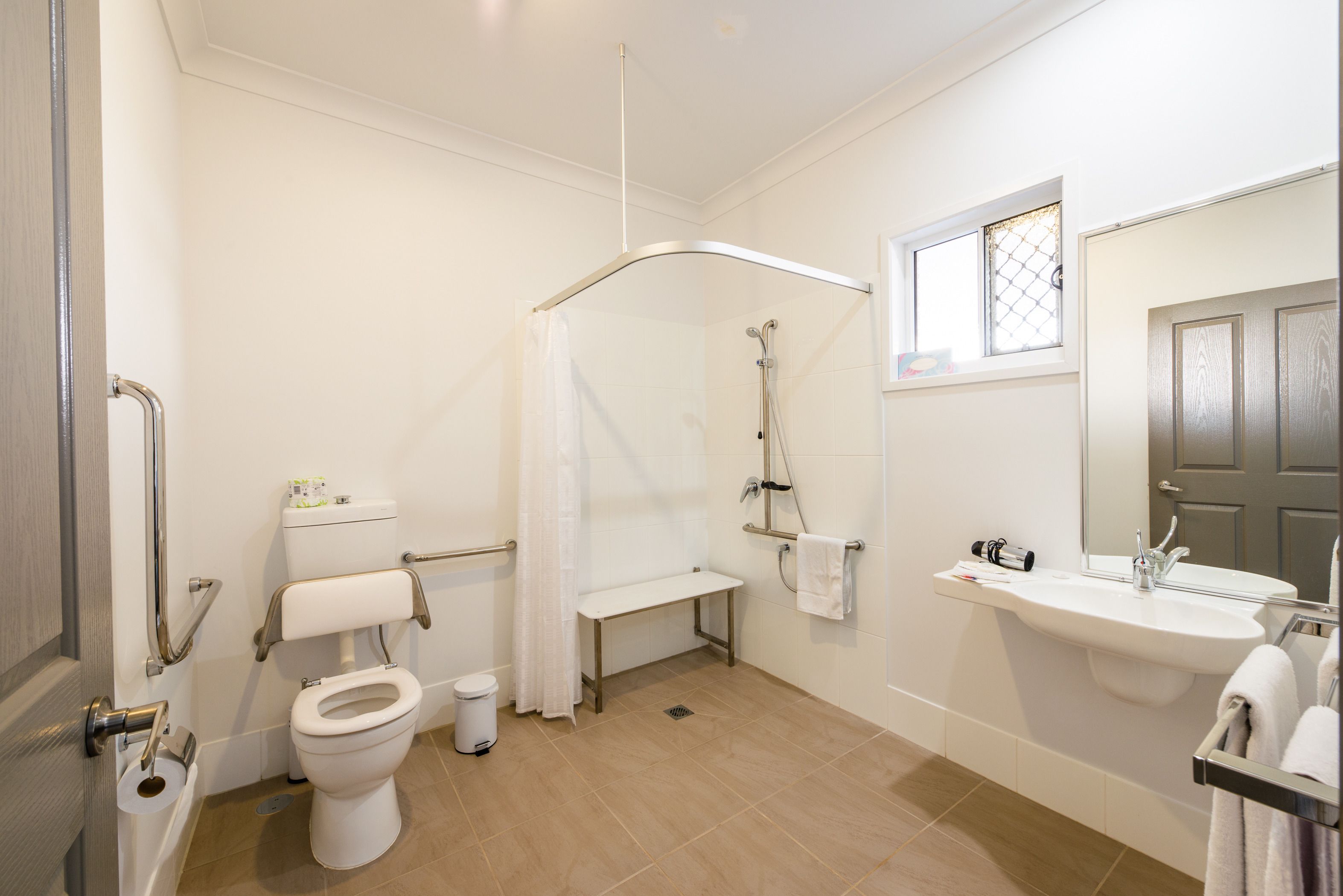 A bathroom with a toilet, shower, sink, and a window.