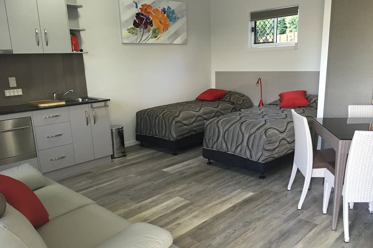 A compact hotel room with two beds, a kitchenette, a dining area, and a window with a view.