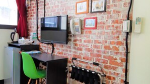 A room with a brick wall, a television, a desk with a chair, a kettle, and a small refrigerator. - LaiChiTe Hotel Love River (Kaohsiung)