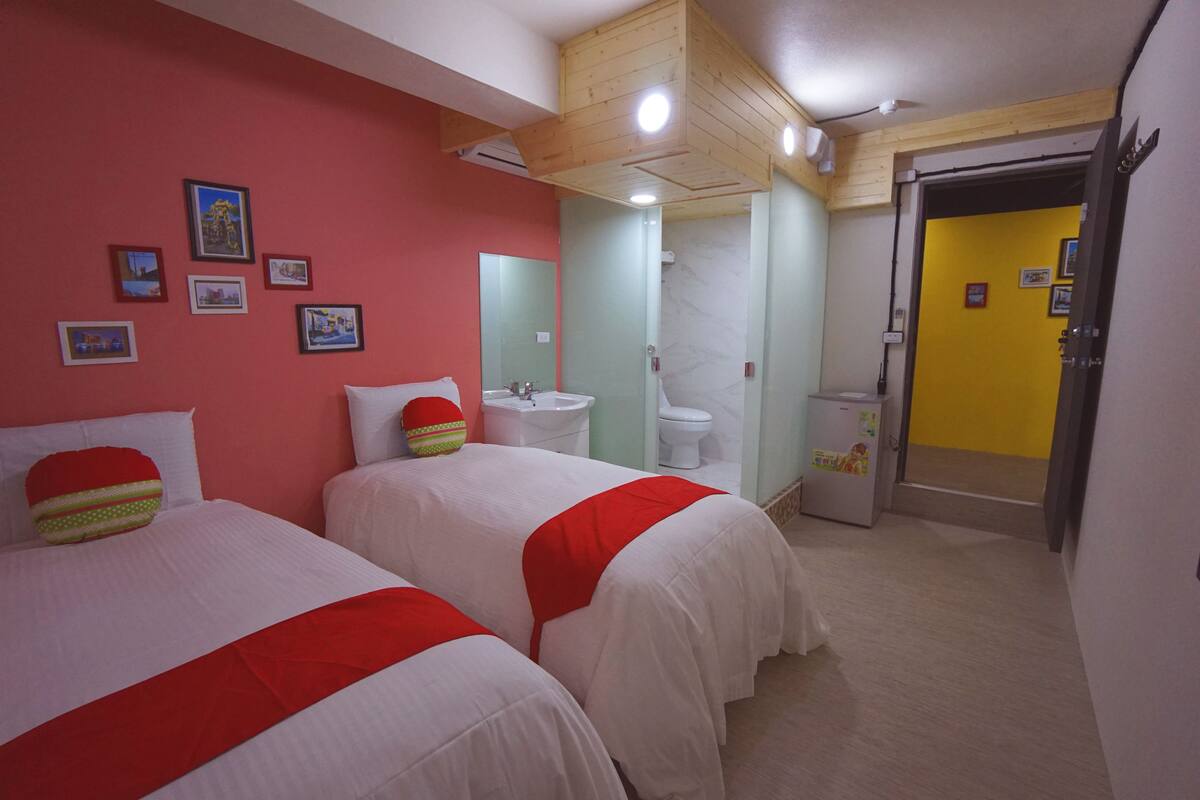 A hotel room with two beds, a bathroom with a sink and toilet, and a door leading to another room.