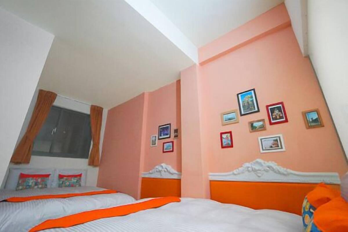 A bedroom with two beds, a window with curtains, and a wall decorated with framed pictures.