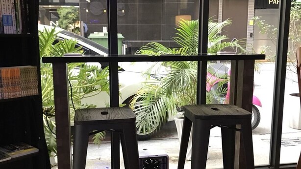 A modern interior with two black bar stools, a bookshelf, and a large window offering a view of the street outside. - LaiChiTe Hotel Love River (Kaohsiung)