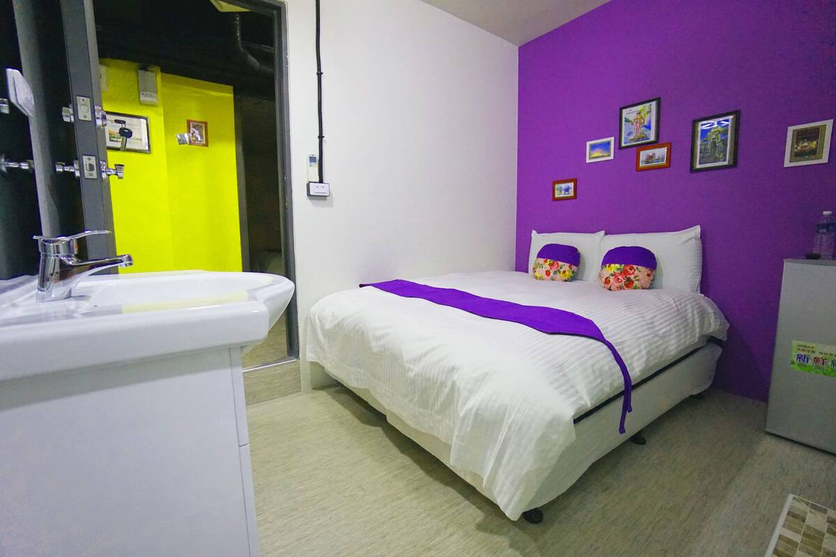 A bedroom with a bed, a nightstand, a dresser, and a bathroom with a sink and mirror.