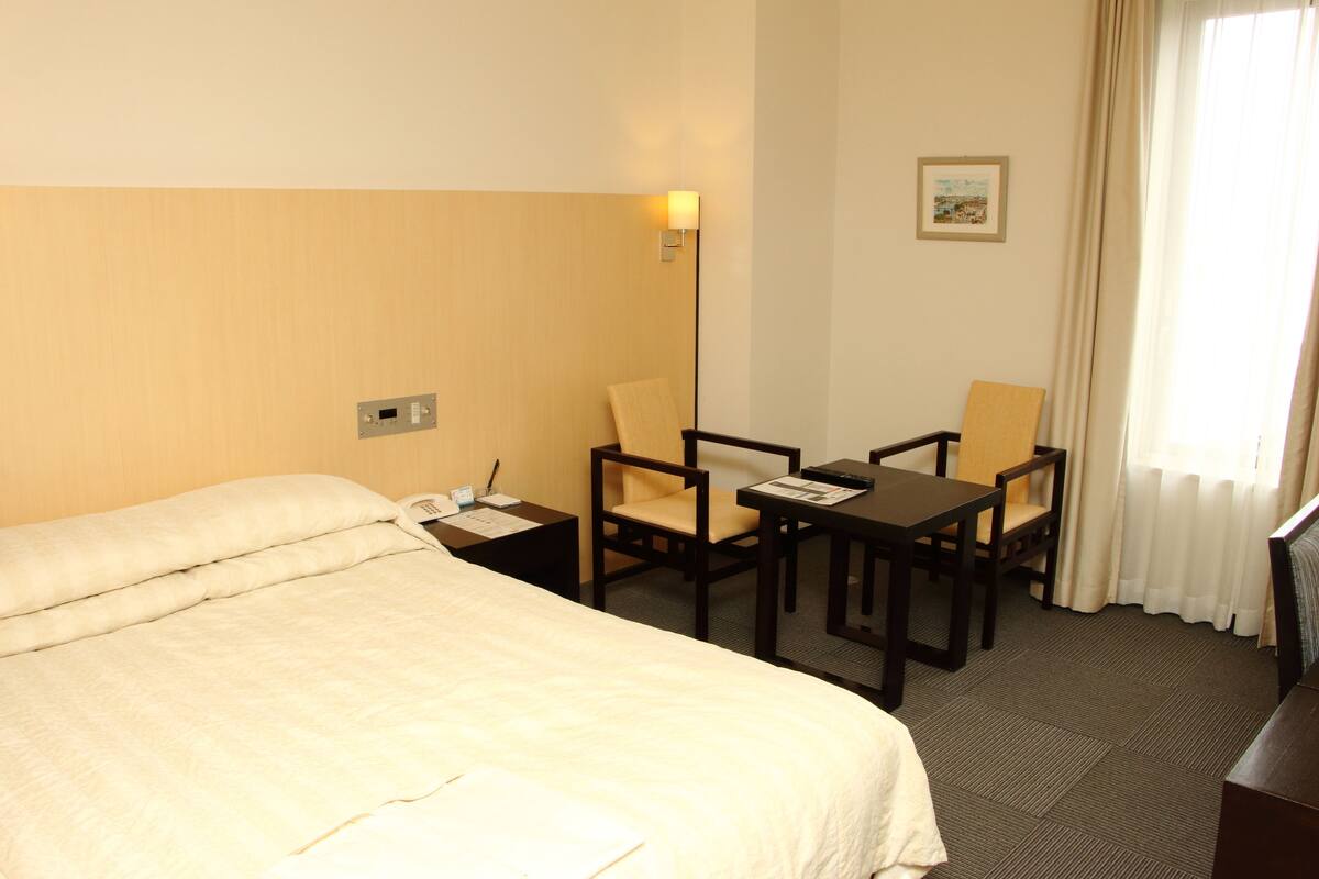 A hotel room with a bed, a desk, two chairs, a lamp, and a picture on the wall.