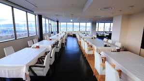 A long dining area with tables and chairs, large windows offering a view of the city, and a black floor. - Winning Hotel (Hakodate)
