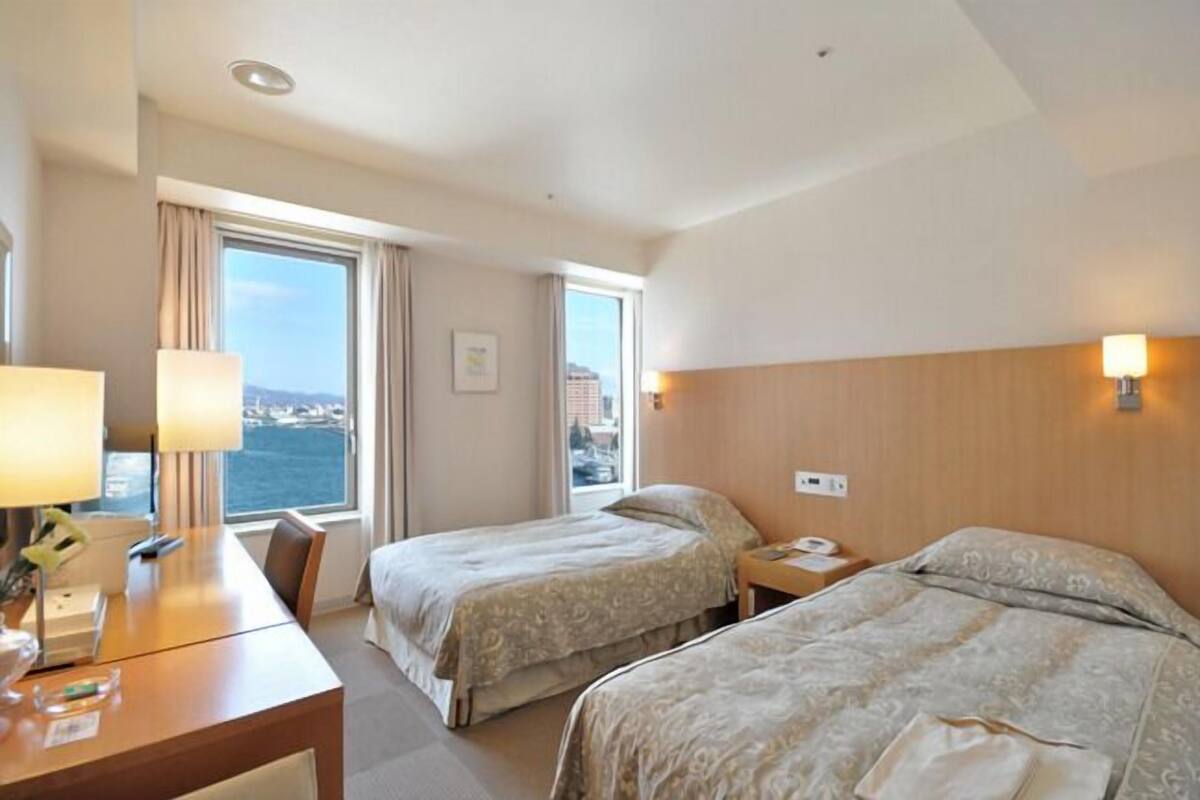 A hotel room with two beds, a desk, and a view of the sea.