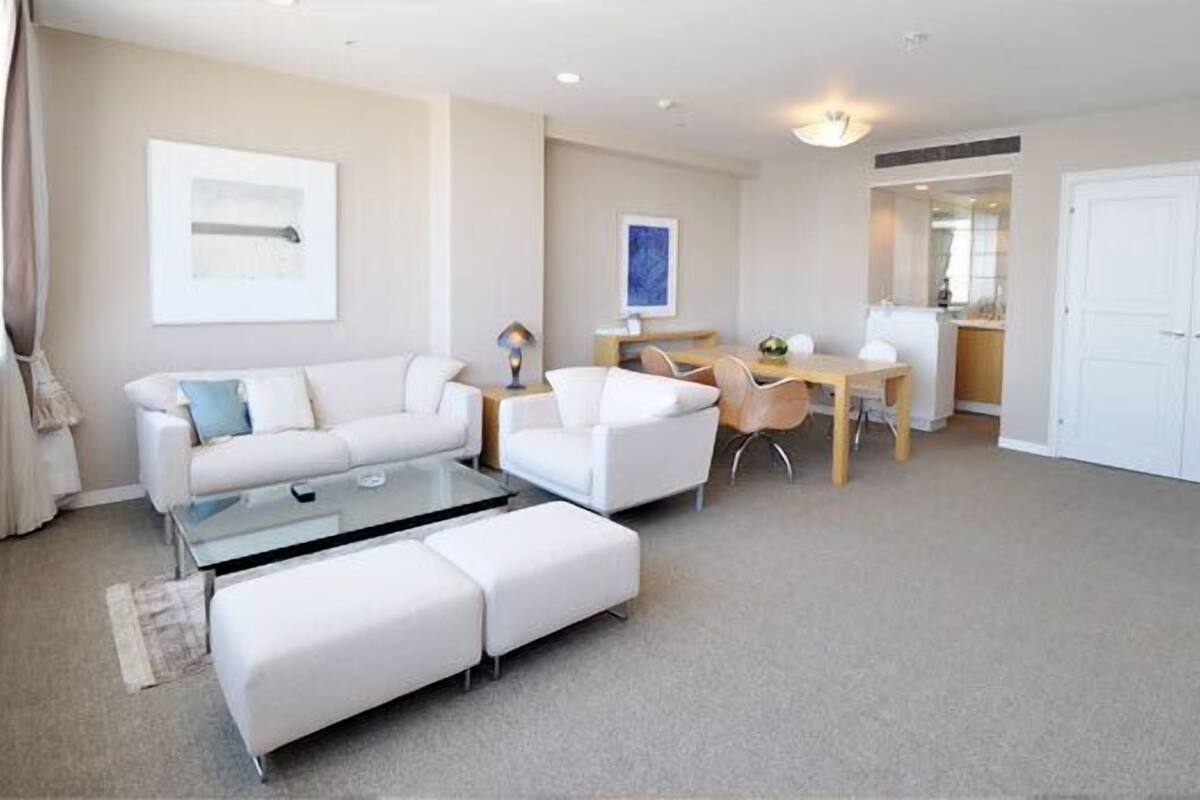 A modern living room with a white sofa, a glass coffee table, and a dining area with a wooden table and chairs.