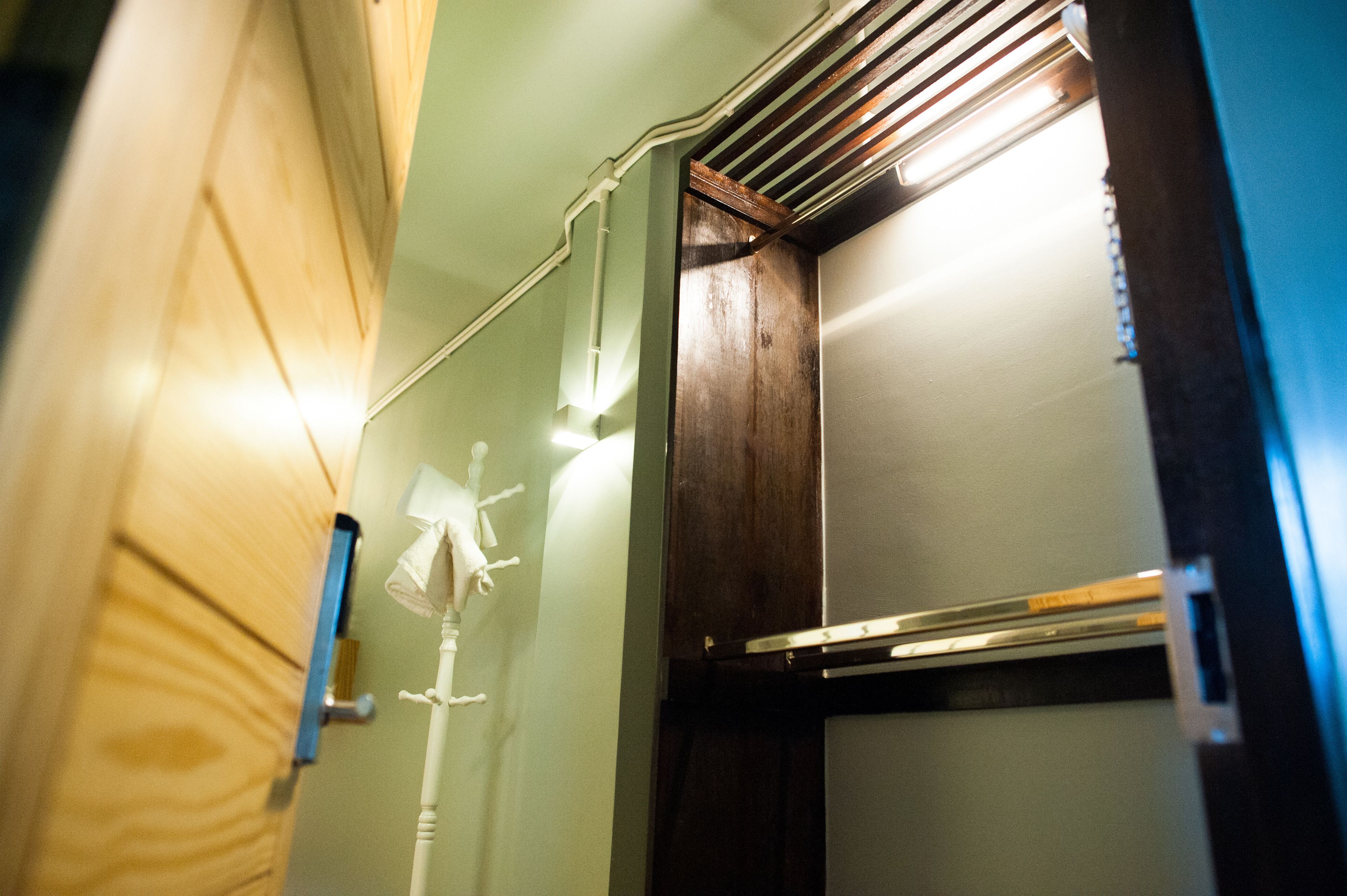 Un coin de pièce avec un lambris en bois, un mur blanc et une grille de ventilation au plafond.