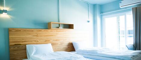 A hotel room with a wooden headboard, two beds, a nightstand, a wall-mounted air conditioner, and a window with blinds.