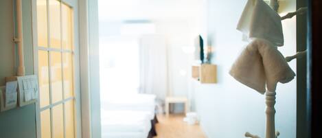 Pasillo de hotel con cama, perchero y lámpara fijada a la pared.