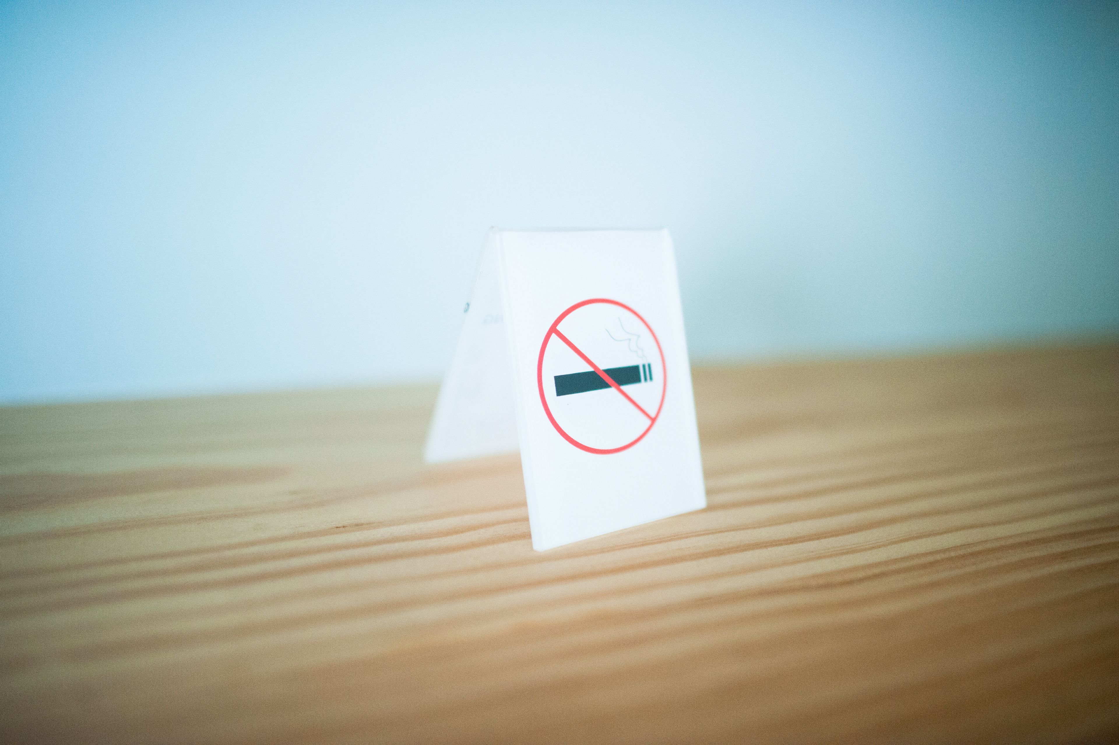 Una señalización de 'no fumar' sobre una tarjeta blanca, colocada sobre una superficie de madera.