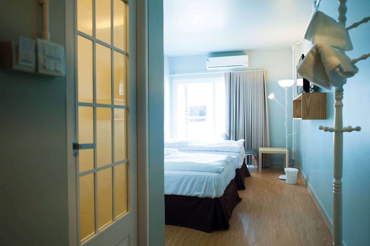 Quarto de hotel com cama, mesa de cabeceira, luminária, aparelho de ar condicionado e janela com cortinas.