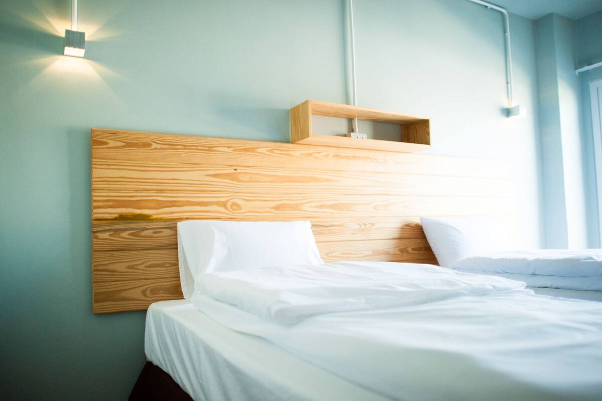 Uma cama bem arrumada em um quarto com cabeceira de madeira e parede em tom claro.