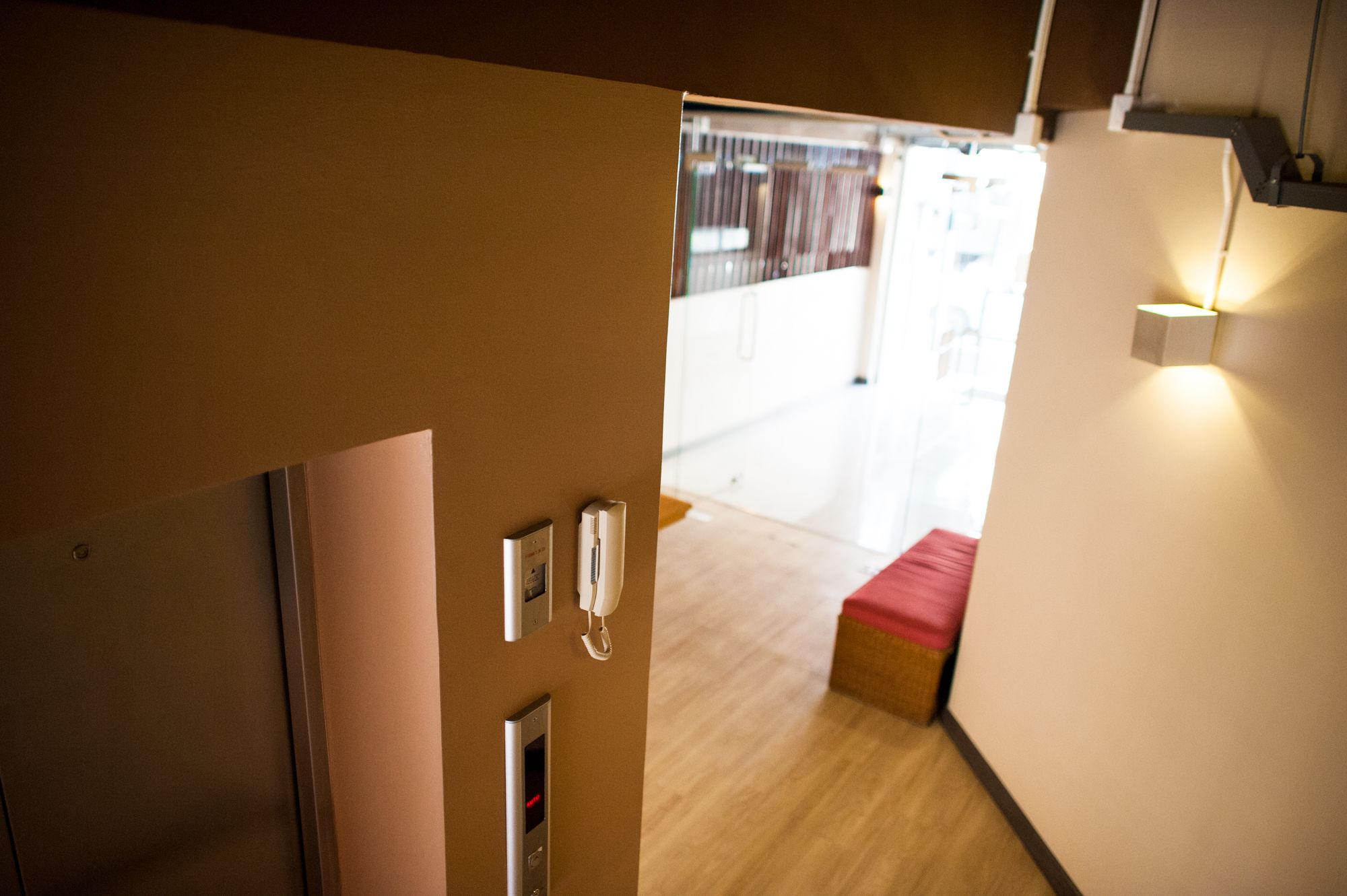 A hotel corridor with a wooden floor, a red bench, and a wall-mounted light fixture.