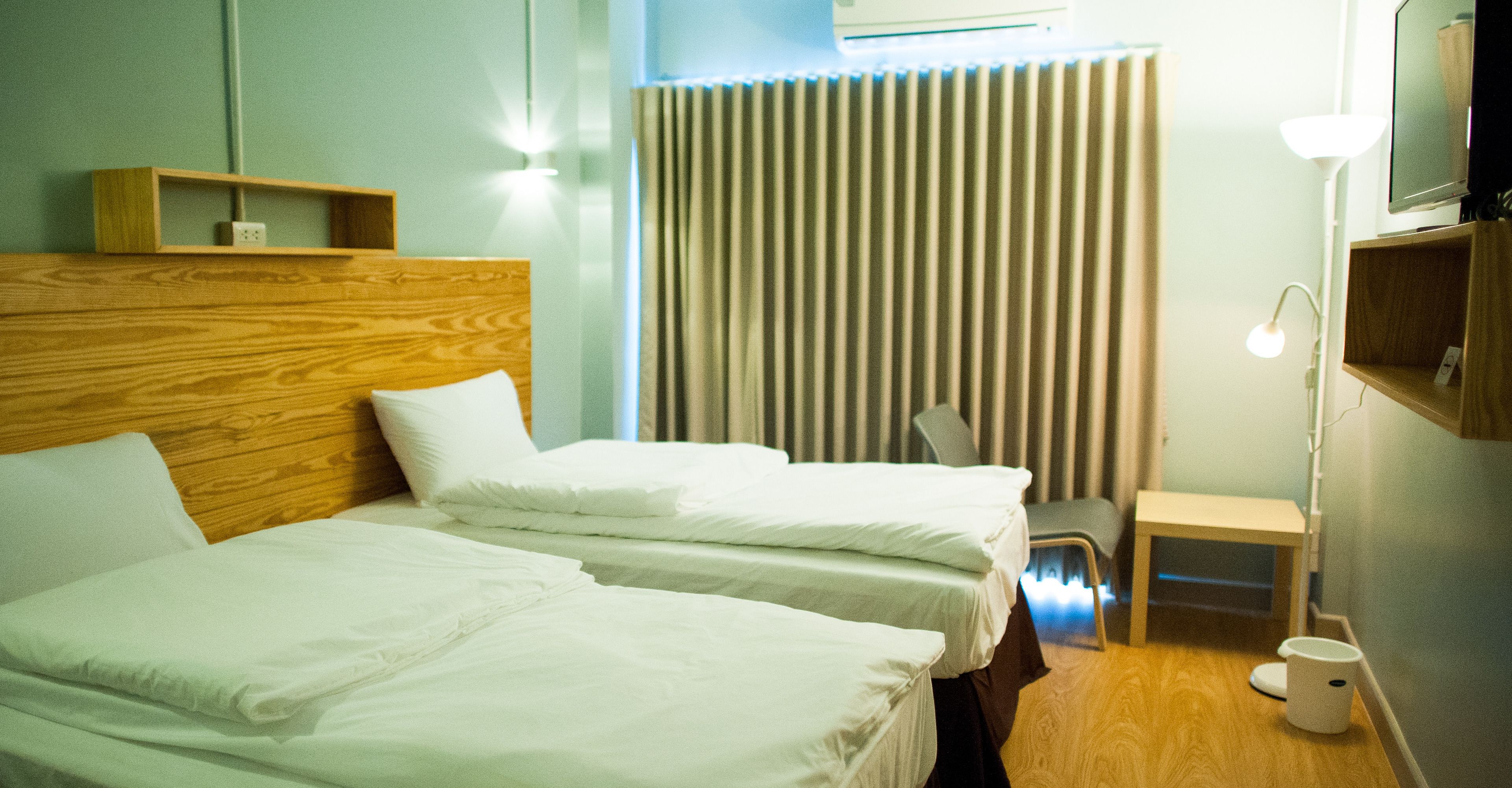 Habitación de hotel con dos camas, un escritorio, una silla, una lámpara y un radiador.