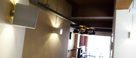 A corridor with a light fixture, a wooden floor, and a view into a room with a table and chairs.