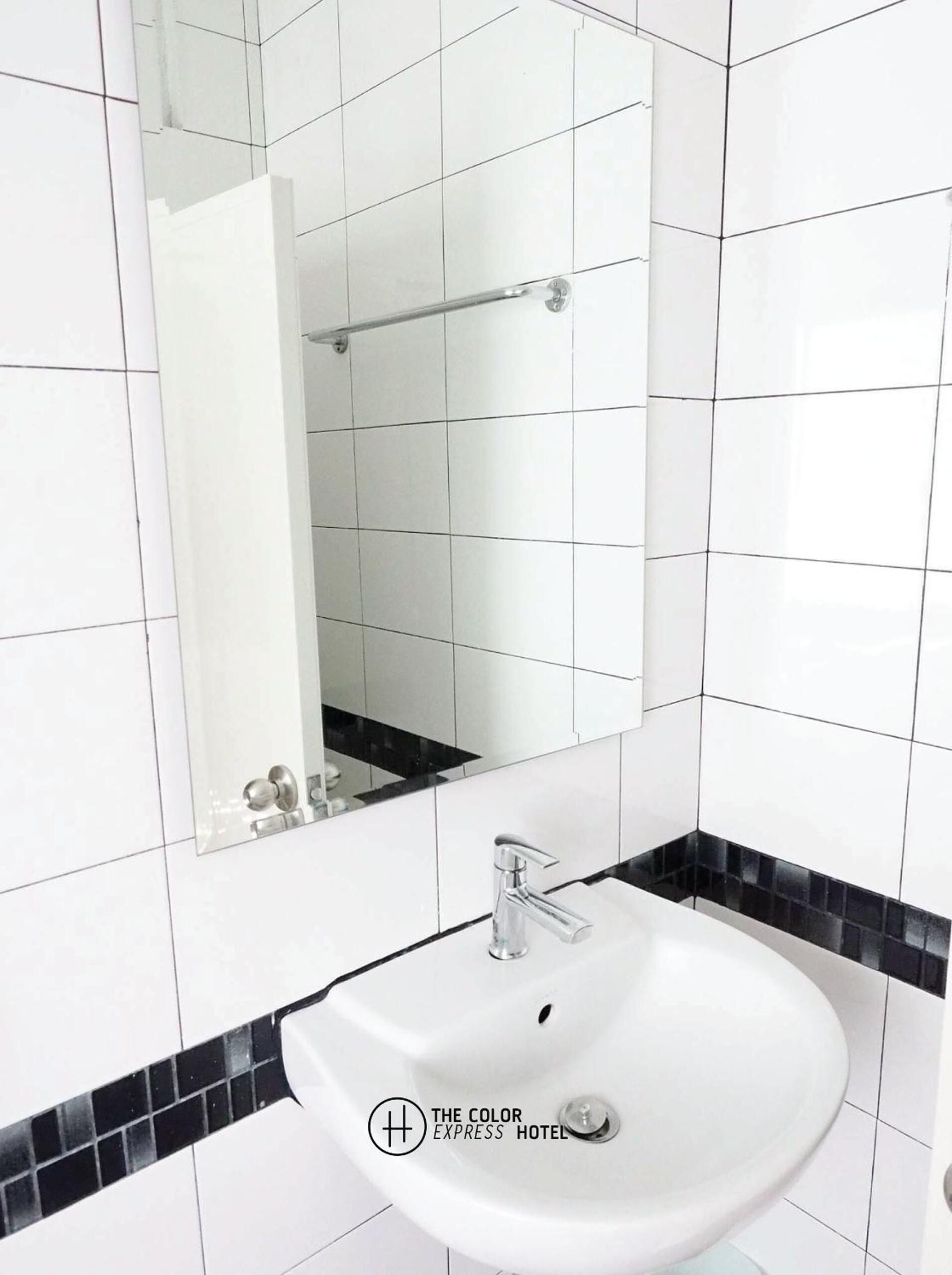 A bathroom with white tiles, a white sink, and a black-tiled accent strip.